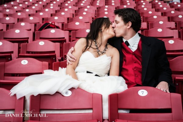 a bride and groom kissing in an empty stadium with red seats